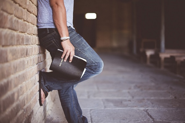 Man leaning against wall with bible